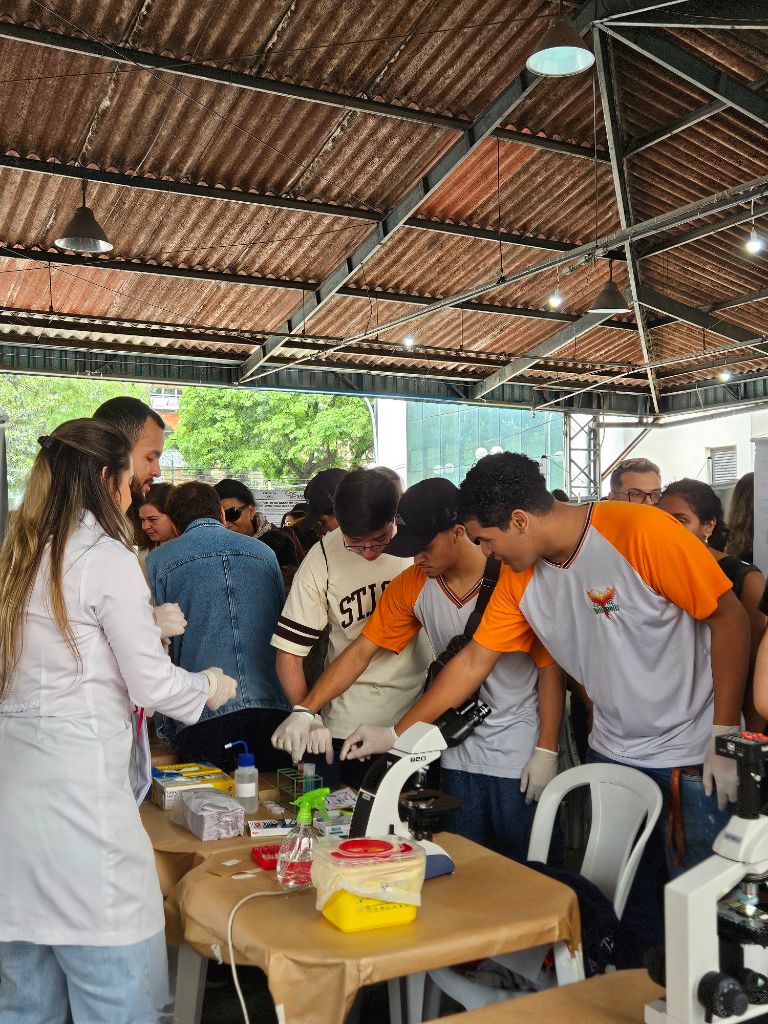 Estudantes realizando experimento com microscópio em estande da I edição, em 2024