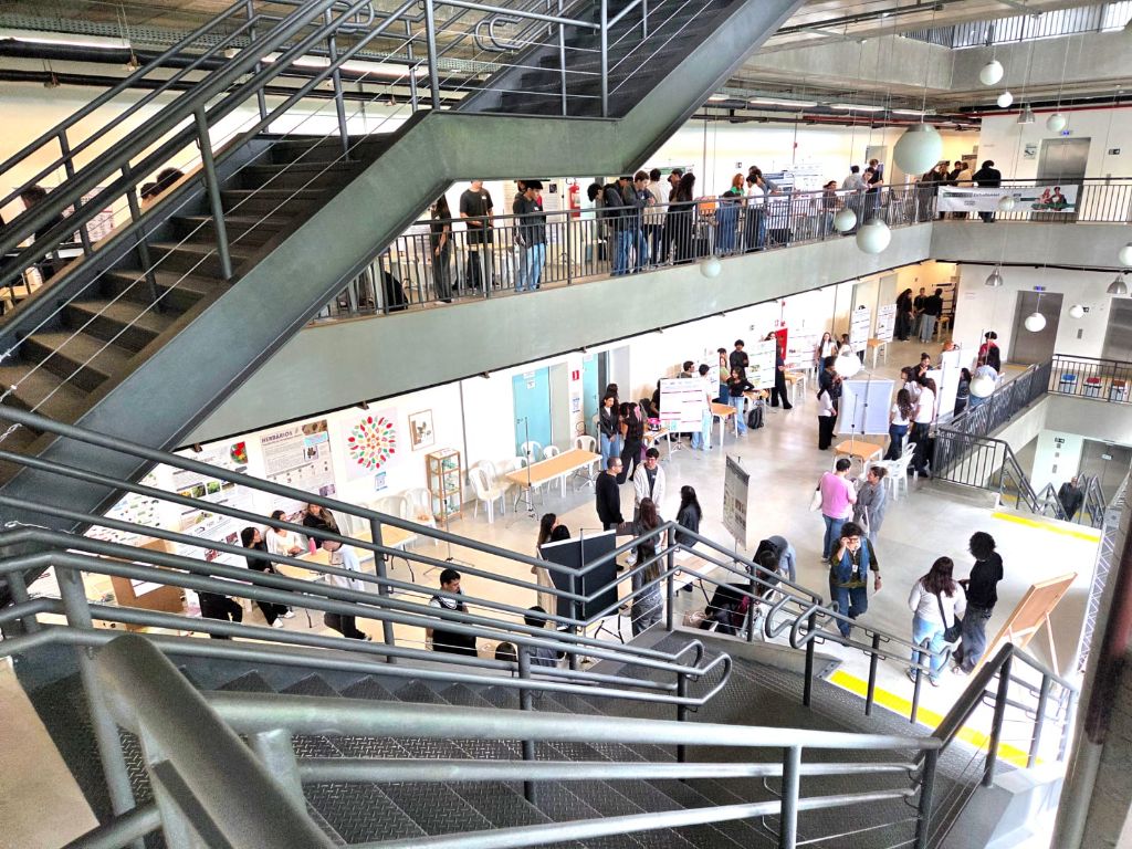 Escadaria e corredores movimentados com estandes de projetos na III edição, em 2026
